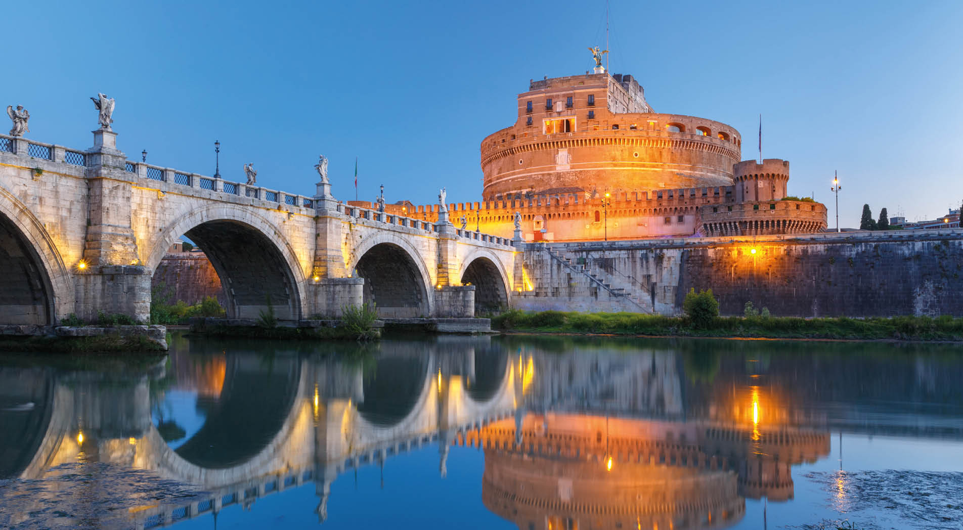 Saint Angel bridge with mirror reflection in Tiber River during morning blue hour in Rome, Italy.