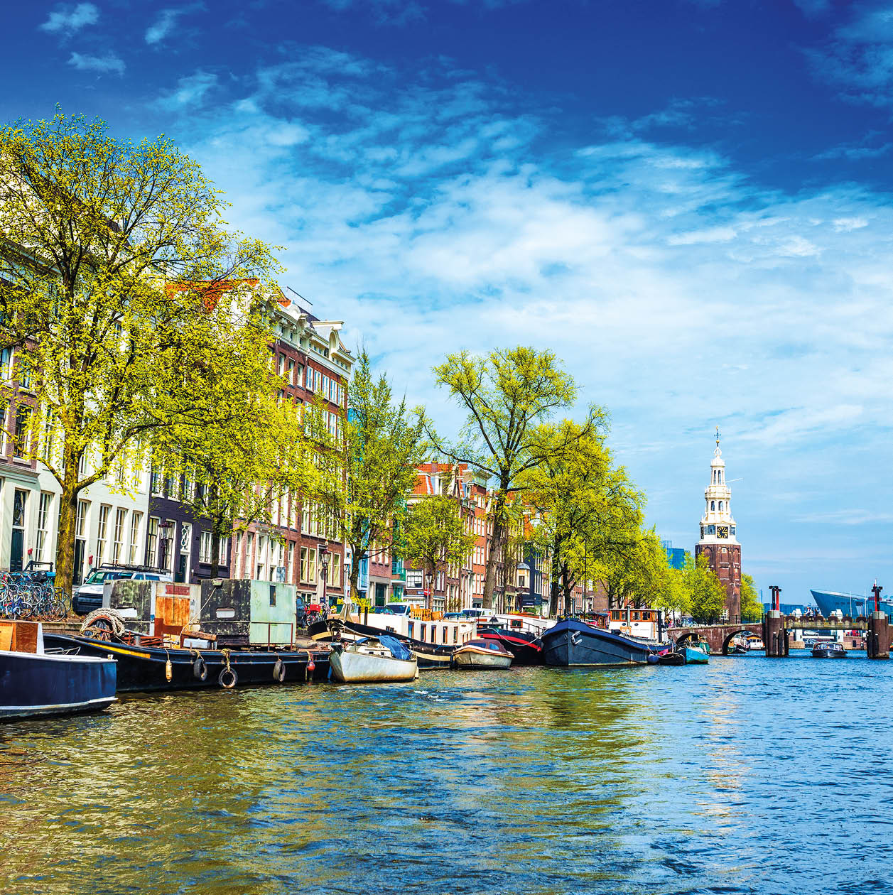 Typical canal in Amsterdam. Visible are restaurants, sightseeing tourism canal boats, typical dutch houses, bridges and Munttoren Tower in Centrum. Amsterdam, Netherlands.