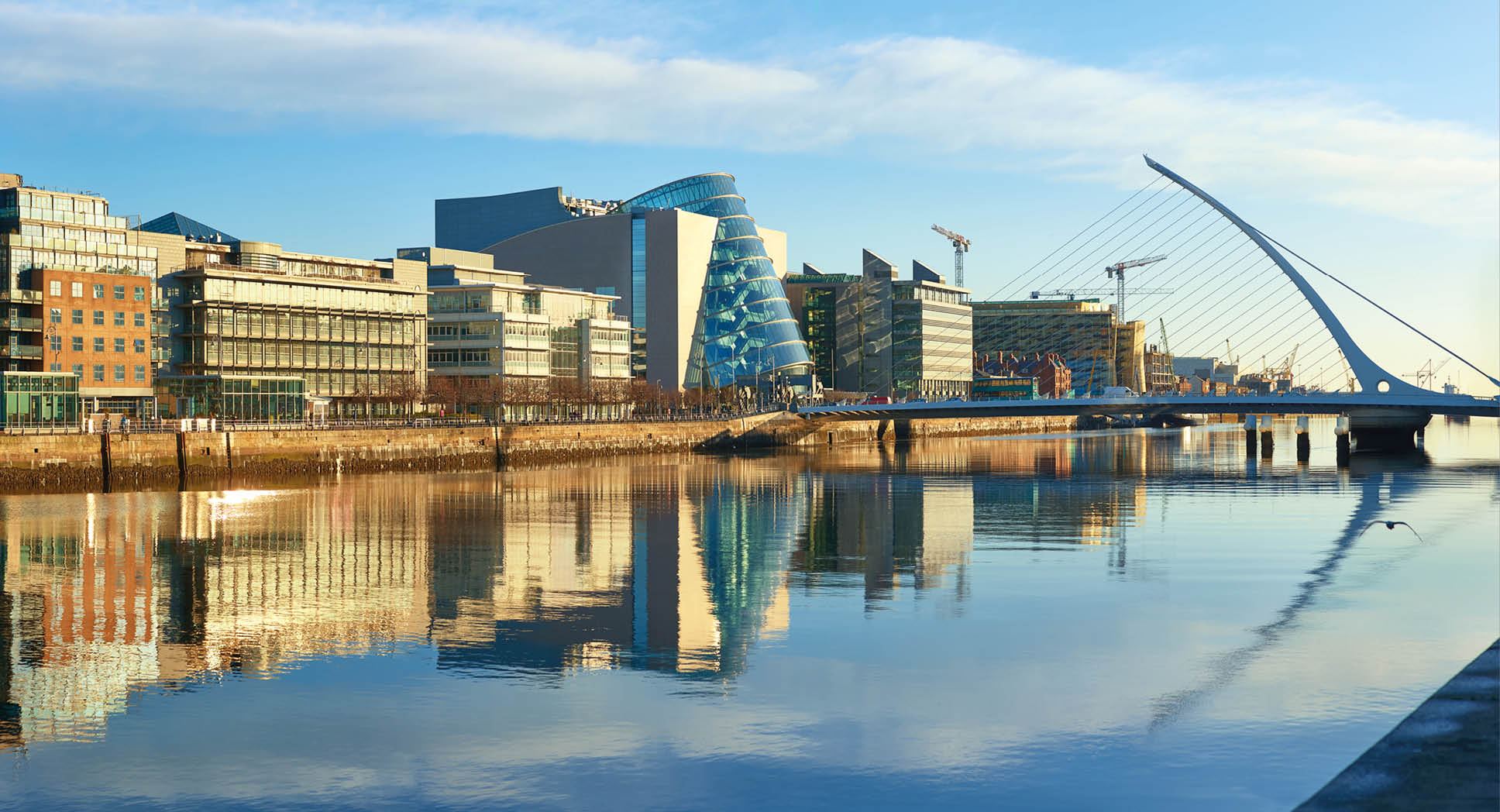 Modern buildings and offices on Liffey river in Dublin on a bright sunny day. Bridge on the right is a famous Harp bridge.