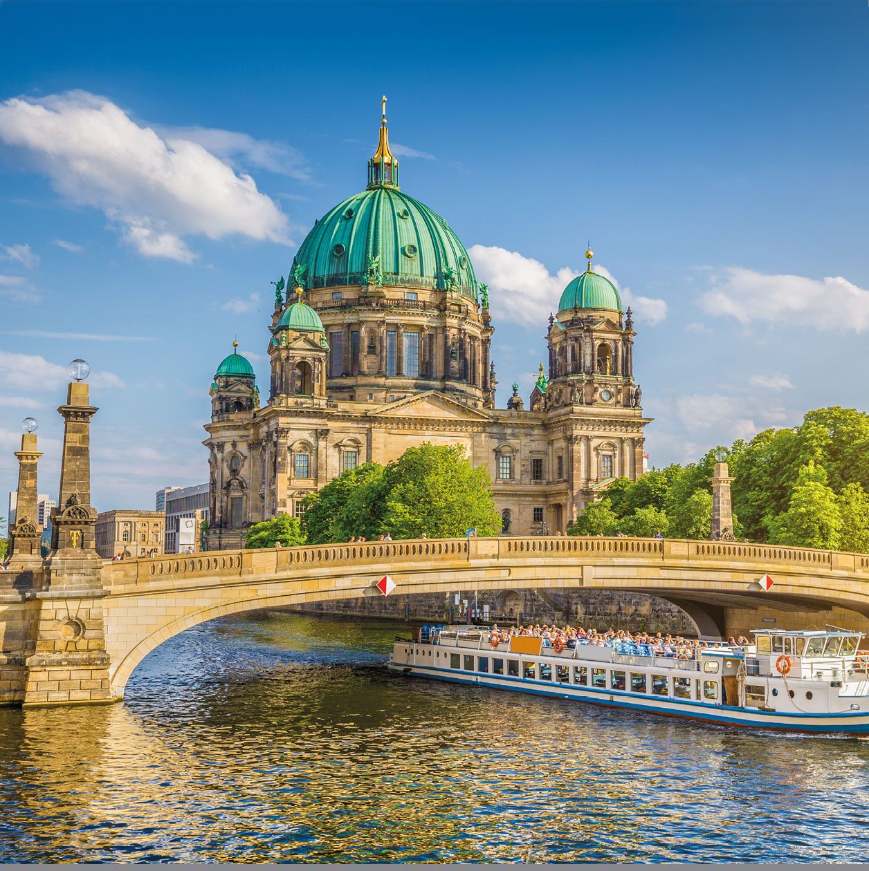 Beautiful view of historic Berlin Cathedral (Berliner Dom) at famous Museum Island with ship passing Friedrichsbrucke bridge on Spree river in golden evening light at sunset in summer, Berlin, Germany