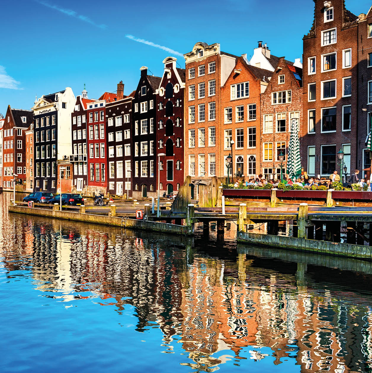 Typical canal in the center of Amsterdam. Visible are restaurants, sightseeing tourism boats at canal (gracht) waterfront and many typical dutch houses in raw and their reflection in the canal. Amsterdam, Netherlands.