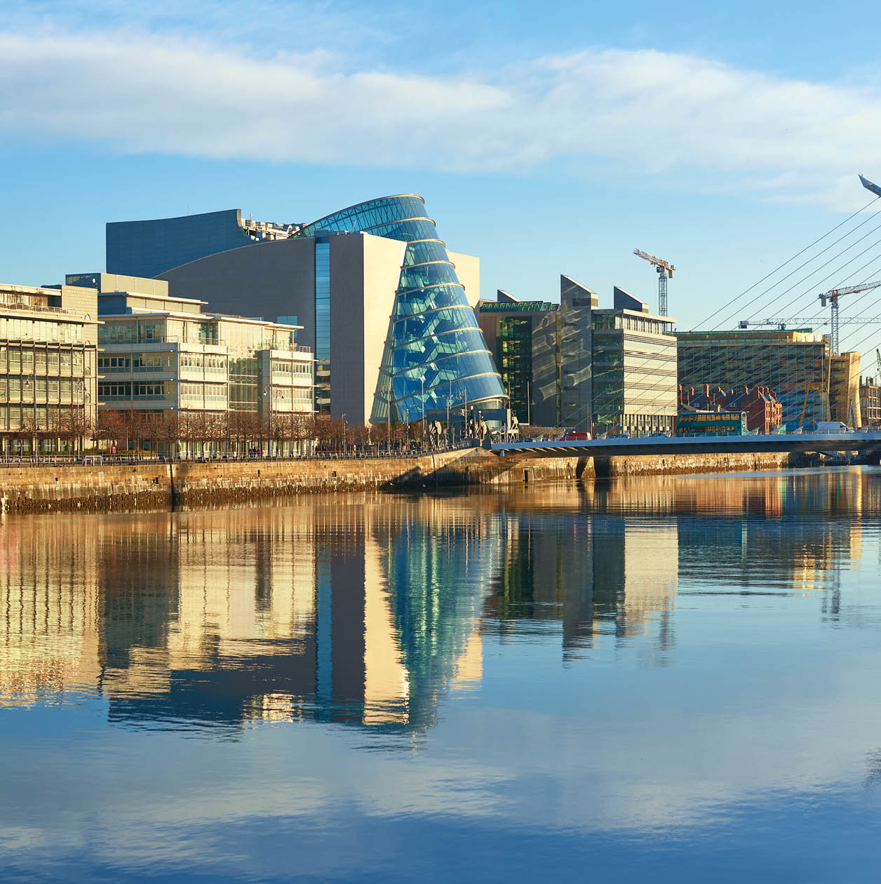 Modern buildings and offices on Liffey river in Dublin on a bright sunny day. Bridge on the right is a famous Harp bridge.