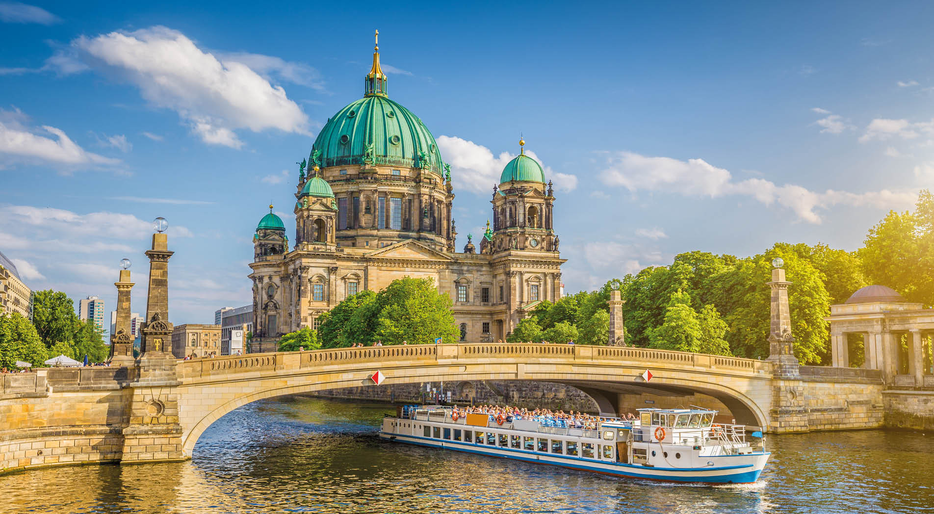 Beautiful view of historic Berlin Cathedral (Berliner Dom) at famous Museum Island with ship passing Friedrichsbrucke bridge on Spree river in golden evening light at sunset in summer, Berlin, Germany