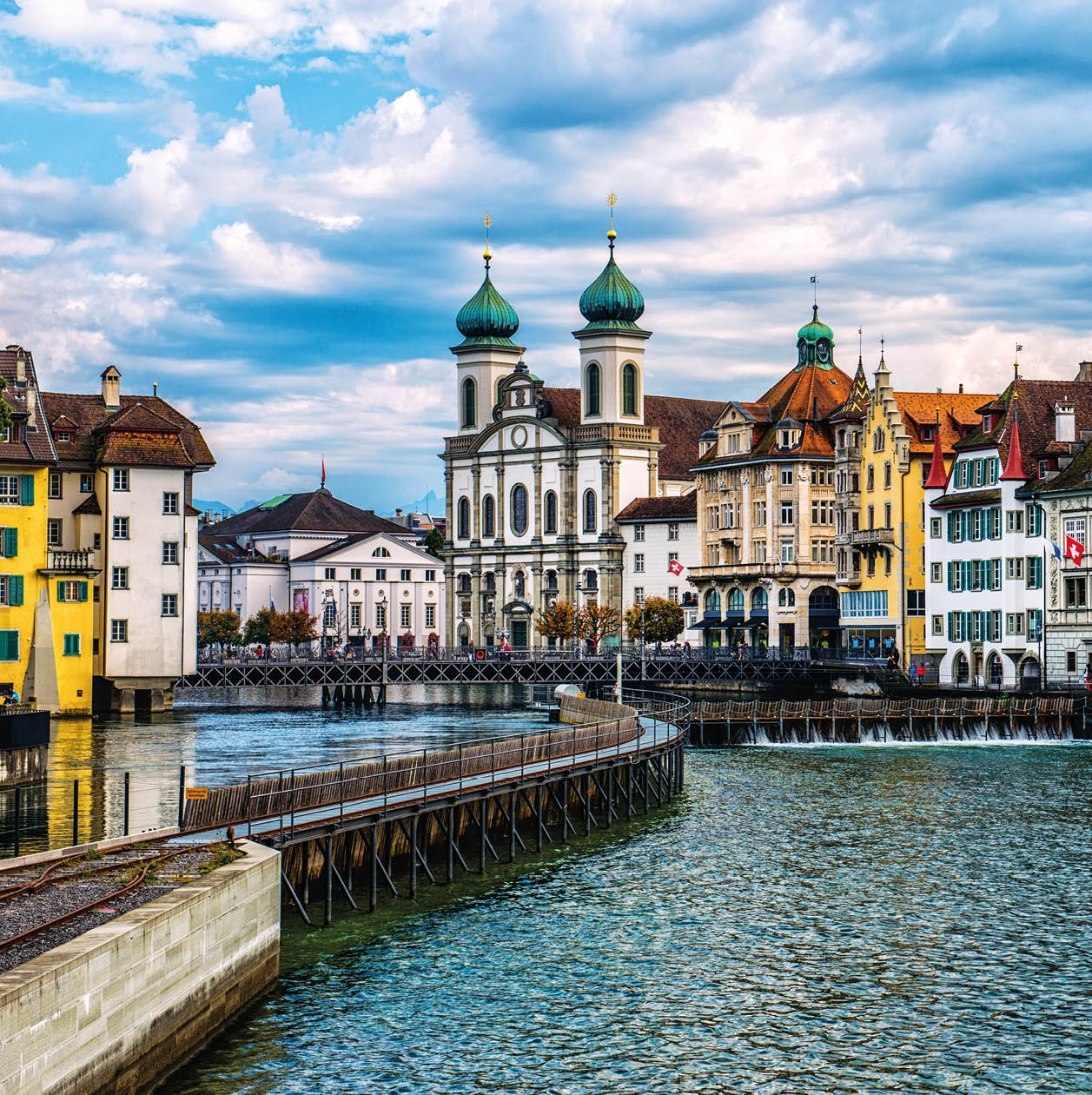 Beautiful Cityscape of old town Lucerne, visible are Jesuit Church, the river Reuss waterfront of Lucerne with the famous Kapellbrucke bridge built in 1333, traditional swiss buildings, restaurants, coffee bars, hotels, beautiful cloudscape and reflection in the water. 