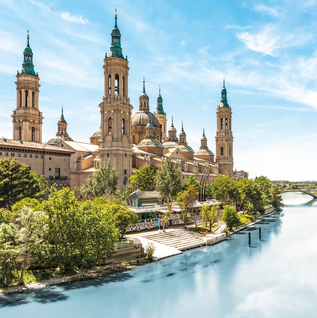 Scenery landscape with Basilica of Our Lady of Pillar. Blue sky reflects in clear water. Green trees along river. Famous church with beautiful architecture. Famous tourist place in Spain, Europe.