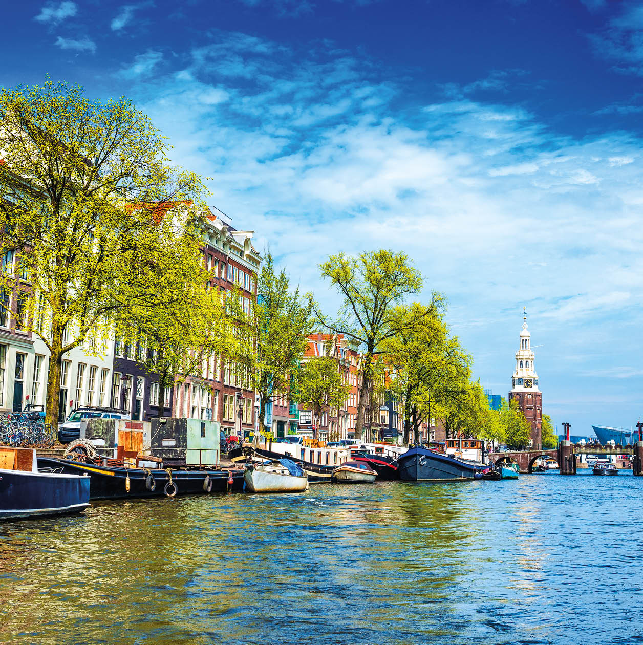 Typical canal in Amsterdam. Visible are restaurants, sightseeing tourism canal boats, typical dutch houses, bridges and Munttoren Tower in Centrum. Amsterdam, Netherlands.