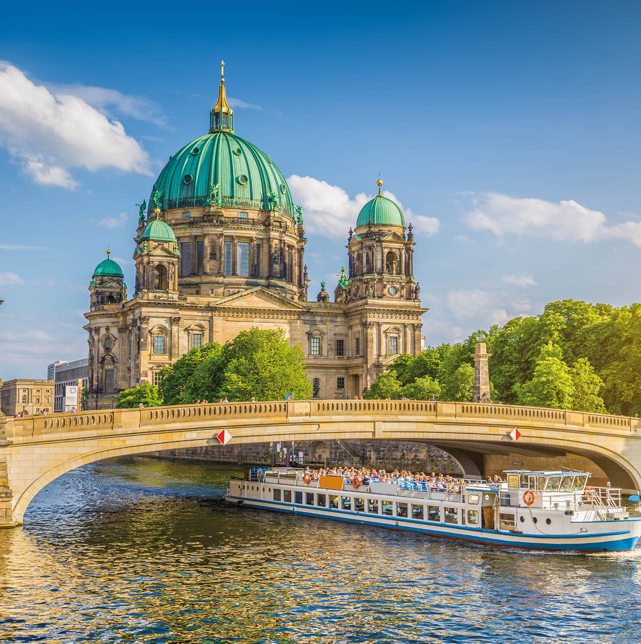 Beautiful view of historic Berlin Cathedral (Berliner Dom) at famous Museum Island with ship passing Friedrichsbrucke bridge on Spree river in golden evening light at sunset in summer, Berlin, Germany