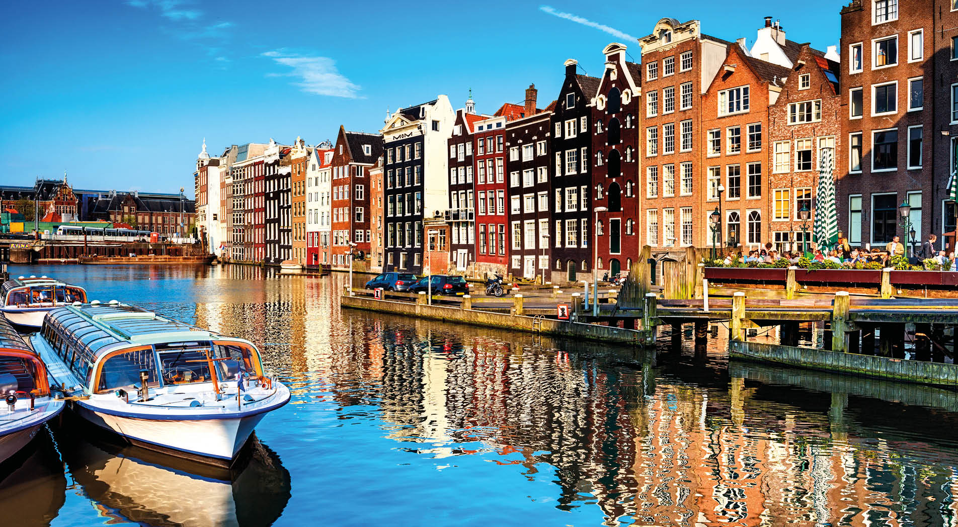 Typical canal in the center of Amsterdam. Visible are restaurants, sightseeing tourism boats at canal (gracht) waterfront and many typical dutch houses in raw and their reflection in the canal. Amsterdam, Netherlands.