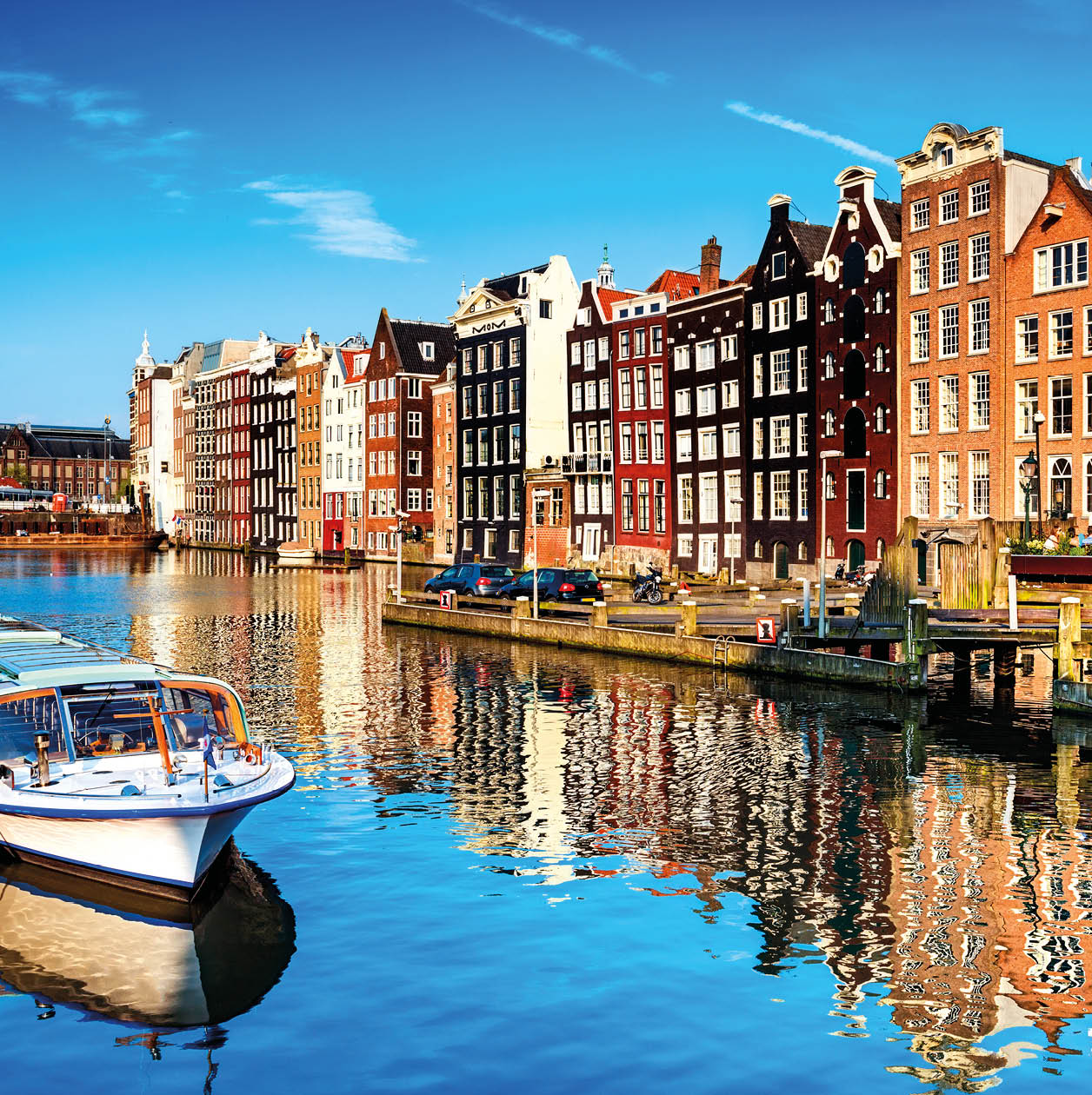 Typical canal in the center of Amsterdam. Visible are restaurants, sightseeing tourism boats at canal (gracht) waterfront and many typical dutch houses in raw and their reflection in the canal. Amsterdam, Netherlands.