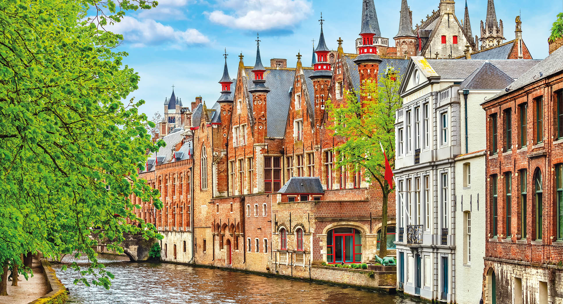 Medieval town Bruges in Belgium. Panorama and landscape vintage channel with old brick house broach on roof. Spring sunny day blue sky white cloud end green trees.